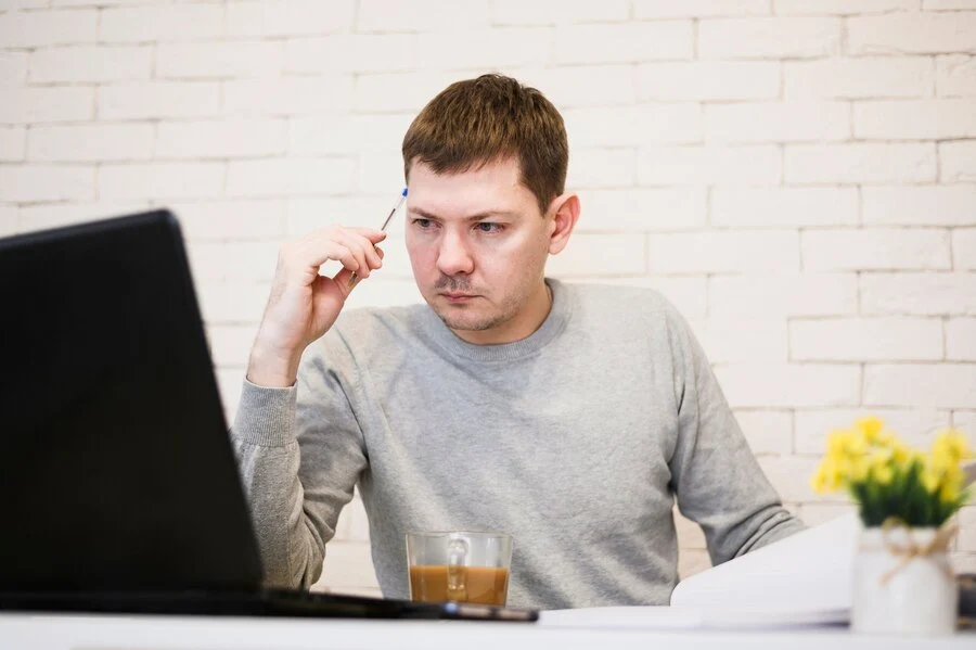 A man sitting at a desk with a laptop, researching about Depression ICD-10.