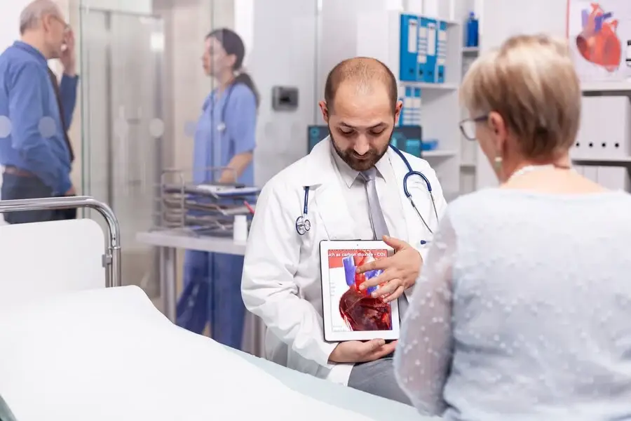 Physician displaying tablet to patient, discussing cardiac catheterization procedure.