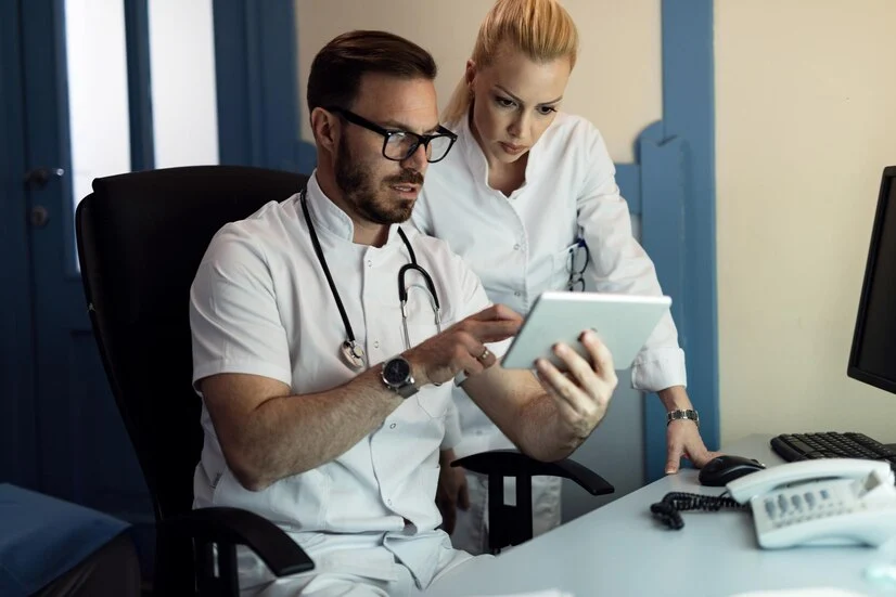 A man and woman in white coats examining a tablet, discussing HIPPA medical billing and coding.